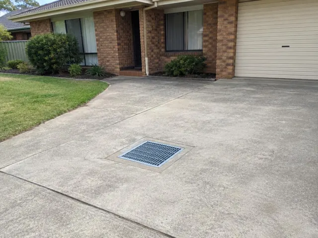 Concrete driveway with a square drain grate outside a brick home in Erskine Park