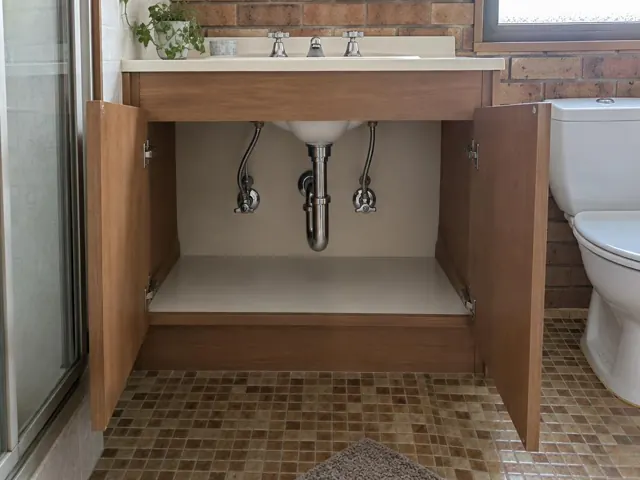 Open bathroom vanity with exposed sink plumbing and dry panel under a tiled wall in St Clair